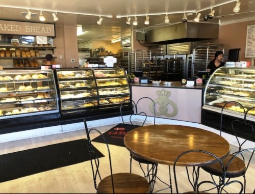 A cozy bakery interior with display cases of pastries, a counter, and a small dining area with a round table and chairs.