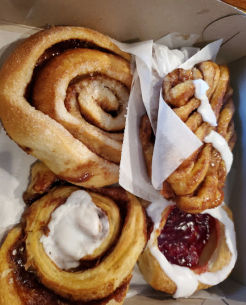 A box of assorted cinnamon rolls and pastries, some with icing and fruit filling, arranged neatly.