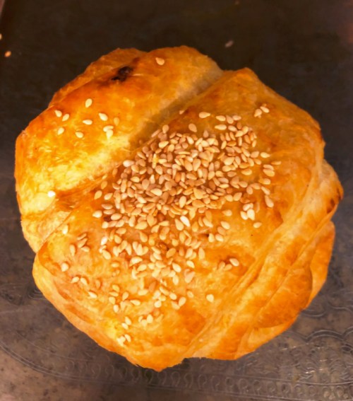 A golden-brown pastry topped with sesame seeds, resting on a textured surface.