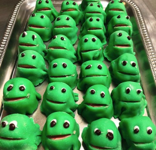 A tray of green frog-shaped treats with smiling faces and large eyes, arranged in neat rows.