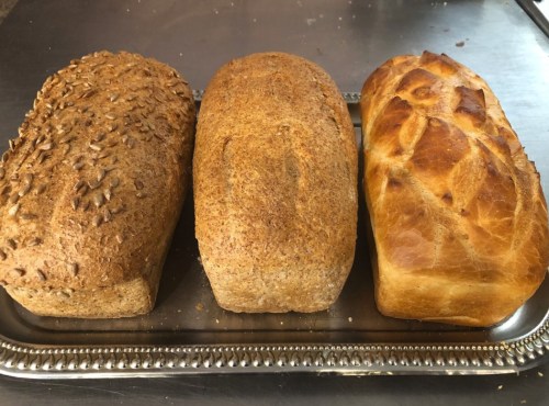 Three loaves of bread on a silver tray: one with seeds, one whole grain, and one with a braided top.