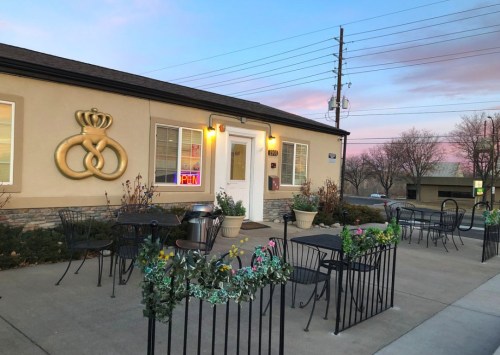 A cozy restaurant exterior with outdoor seating, featuring a large decorative emblem and a colorful sunset sky.