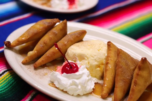 A plate of fried pastries with ice cream, whipped cream, and a cherry, set on a colorful striped tablecloth.