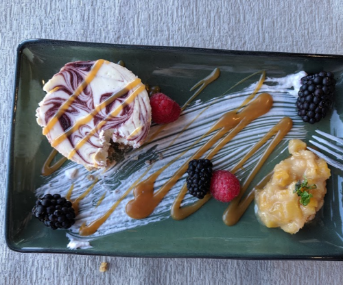 A dessert plate featuring a marbled cake, berries, caramel drizzle, and a dollop of fruit compote on a green dish.