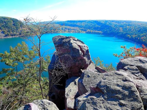 A scenic view of a blue lake surrounded by green trees and rocky cliffs under a clear sky.