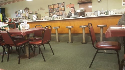 A cozy diner interior with empty tables and a waitress behind the counter preparing food.