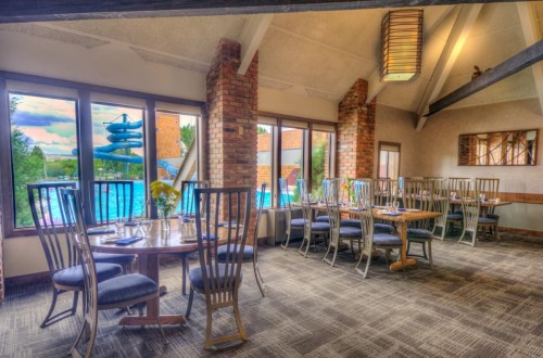 A dining area with wooden tables and chairs, large windows overlooking a pool with a water slide.