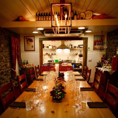 A cozy dining room with a long wooden table set for a meal, surrounded by stone walls and warm lighting.