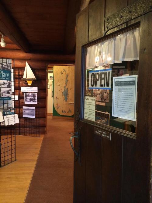 A wooden door with an "OPEN" sign leads into a cozy museum with exhibits and displays visible inside.