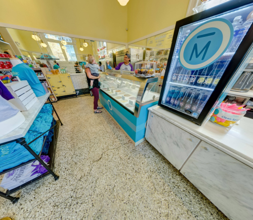 A colorful ice cream shop interior with a customer at the counter and a display of ice cream flavors.
