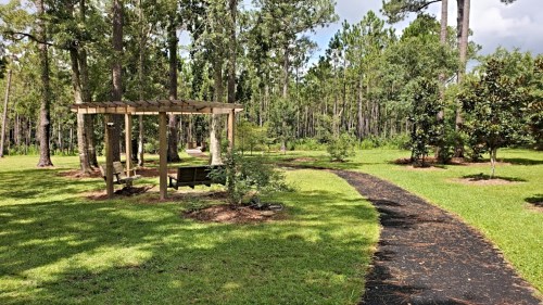 A serene park scene featuring a wooden gazebo, a winding path, and lush greenery surrounded by tall trees.