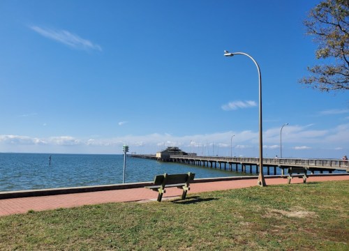 A peaceful waterfront scene featuring a pier, benches, and clear blue skies over calm water.