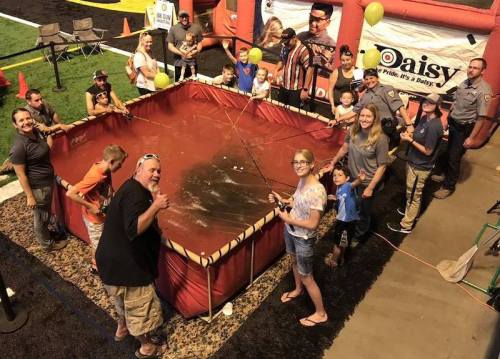 A group of people, including children, gather around a large inflatable fishing pond, smiling and holding fishing rods.
