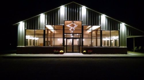 A modern building at night, illuminated with lights, featuring large windows and a welcoming entrance.