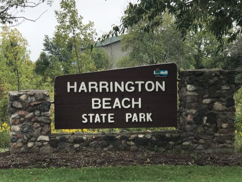 Sign for Harrington Beach State Park, featuring stone base and wooden lettering, surrounded by greenery.