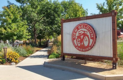 Sign for New Belgium Brewing with a bicycle logo, surrounded by greenery and a pathway leading to the brewery.
