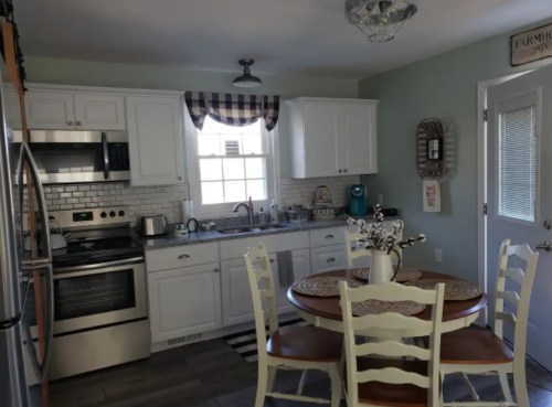 A cozy kitchen with white cabinets, stainless steel appliances, a round table, and a checkered curtain.