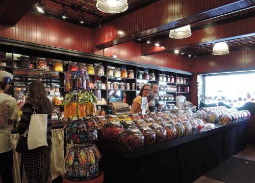 A colorful candy store with jars of sweets, shelves filled with treats, and customers at the counter.