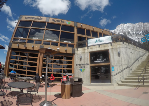 Exterior view of Creekside Sports and Cafe, featuring large windows, outdoor seating, and a mountain backdrop.