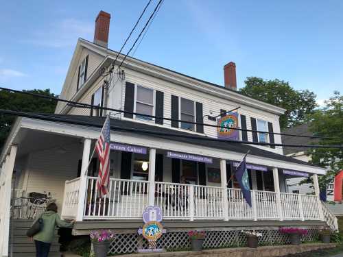 A white two-story building with a porch, featuring signs for ice cream and a homemade waffle shop, surrounded by trees.