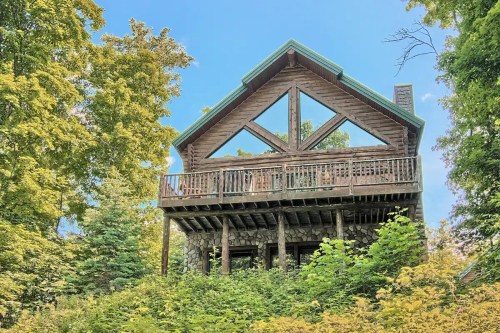 A large wooden cabin surrounded by lush green trees under a clear blue sky.