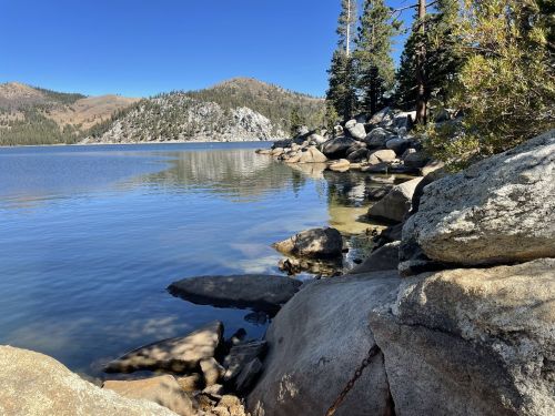 A serene lake surrounded by rocky shores and pine trees under a clear blue sky.