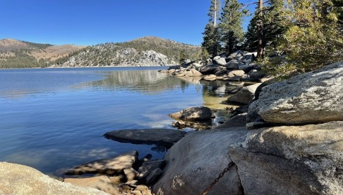 A serene lake surrounded by rocky shores and pine trees under a clear blue sky.