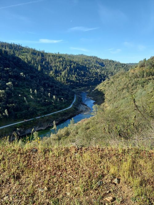 A scenic view of a winding river surrounded by lush green hills under a clear blue sky.
