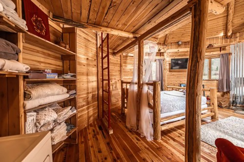 Cozy wooden interior of a cabin featuring a bed, shelves with linens, and a ladder leading to a loft area.