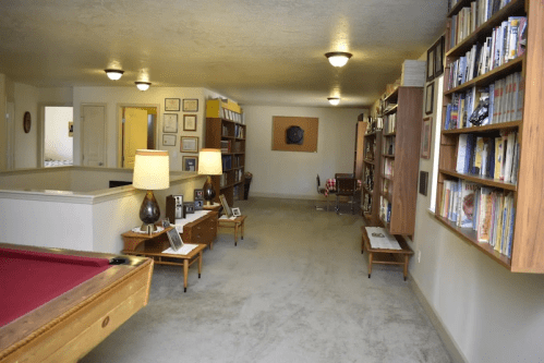 A spacious room with a pool table, bookshelves, lamps, and framed pictures on the walls.