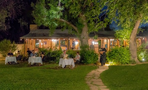 A cozy outdoor restaurant at night, with diners at tables surrounded by greenery and warm lighting.