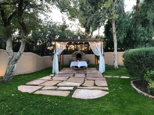 A serene outdoor setting with a stone pathway leading to a gazebo draped in white fabric, surrounded by greenery.