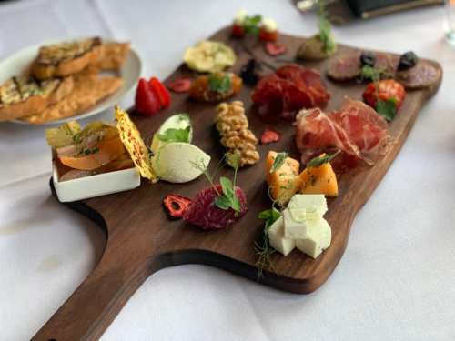 A wooden platter filled with assorted cheeses, meats, fruits, nuts, and garnishes, elegantly arranged for serving.