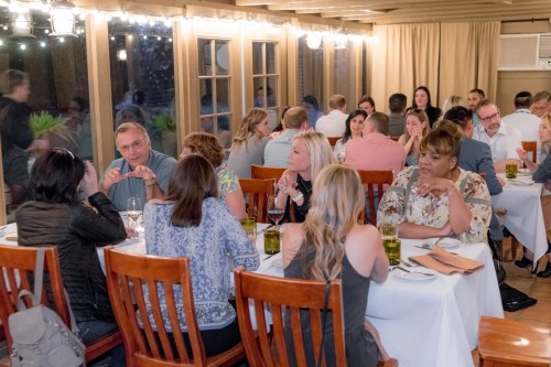 A lively restaurant scene with groups of people dining and chatting at tables, illuminated by warm string lights.