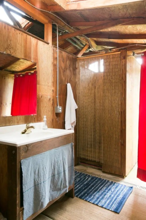 A rustic bathroom with wooden walls, a sink, a shower with red curtains, and a bamboo screen.