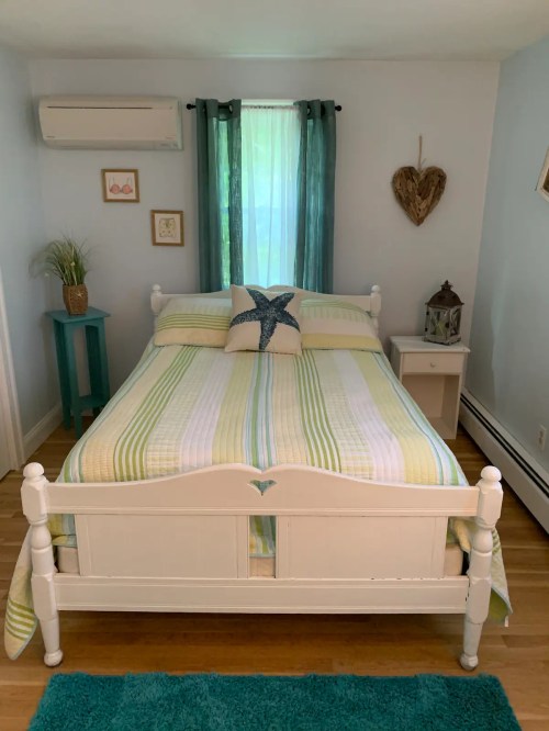 Cozy bedroom featuring a white bed with striped bedding, teal accents, and natural light from a window.