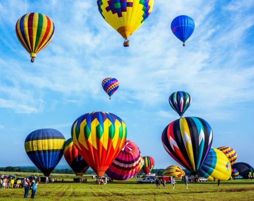 A vibrant scene of colorful hot air balloons ascending against a blue sky, with people gathered on the ground.