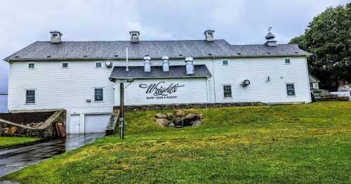 A white barn with "Wright's Dairy Farm & Bakery" painted on the side, set on a grassy area under a cloudy sky.