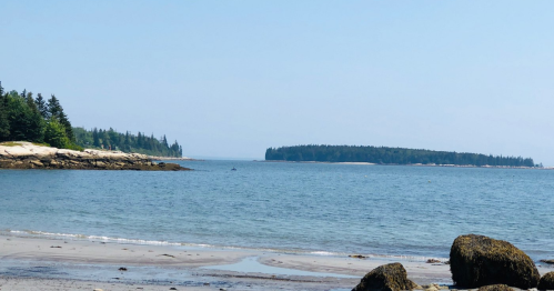 A serene coastal view featuring calm waters, sandy shore, and distant islands under a clear blue sky.