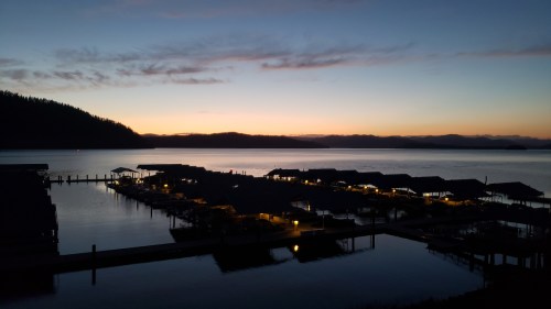 A serene lakeside view at dusk, with silhouetted docks and soft lights reflecting on the water.