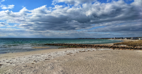 A serene beach scene with sandy shore, gentle waves, and a cloudy sky in the background.