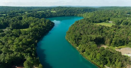 Aerial view of a winding river surrounded by lush green forests and rolling hills under a clear blue sky.