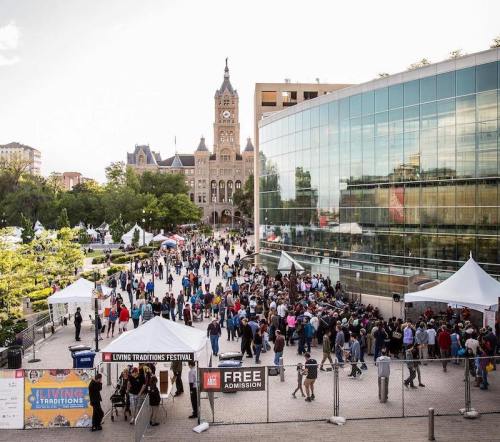 A bustling outdoor festival with crowds, tents, and a historic building in the background under a clear sky.
