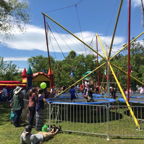 A lively outdoor scene with people enjoying a trampoline attraction and colorful inflatable structures in a park.