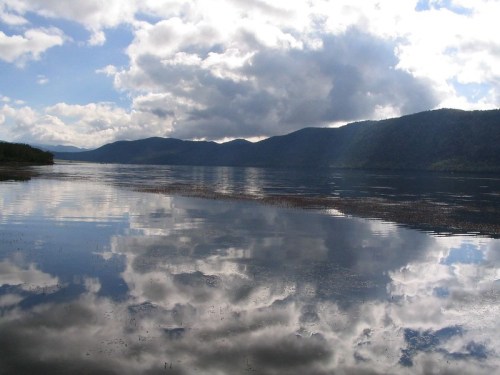 A serene lake reflecting clouds and mountains under a blue sky, creating a tranquil and picturesque landscape.