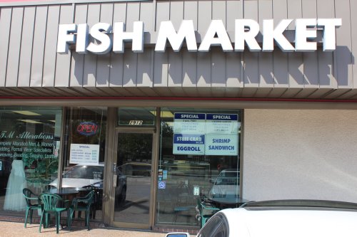 Exterior of a fish market with a large sign, open door, and menu displayed in the windows.