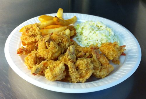 A plate of fried shrimp, French fries, and coleslaw on a white paper plate.