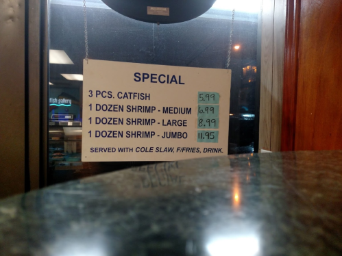 Menu sign displaying seafood specials: catfish, medium, large, and jumbo shrimp with prices listed.