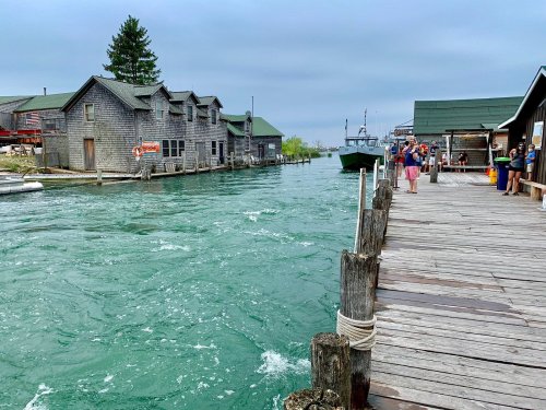 A wooden dock beside a turquoise waterway, with rustic buildings and people enjoying the waterfront scene.