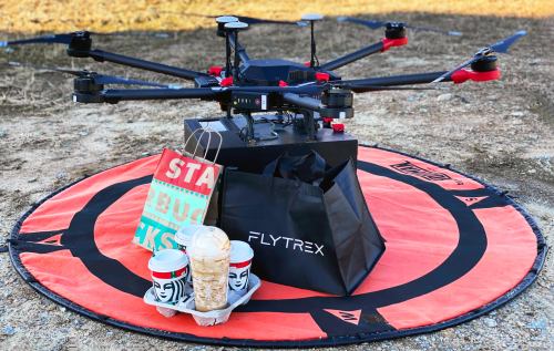 A drone on a landing pad with a delivery bag and drinks, ready to deliver food.